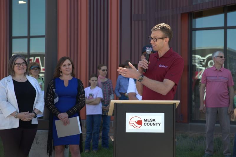 Man standing outside at lectern holding a mic to his mouth. 