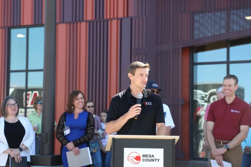  Man standing outside at lectern holding a mic to his mouth. 