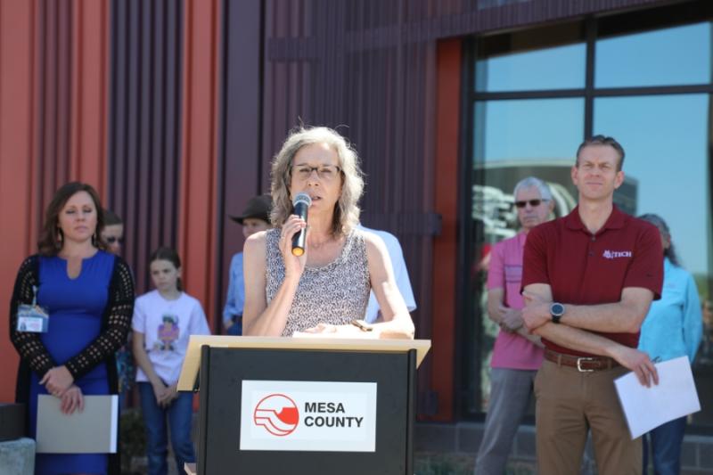 Woman standing outside at lectern holding a mic to her mouth. 