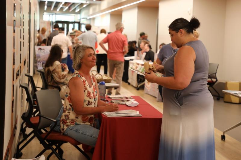 Woman standing at booth talking to a woman sitting at a table. 