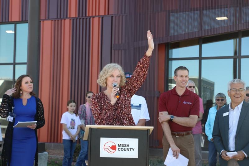 Woman standing outside at a lectern with her hand raised. 