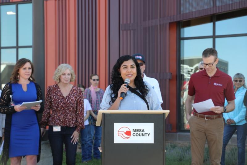 Woman standing outside at lectern holding a mic to her mouth. 