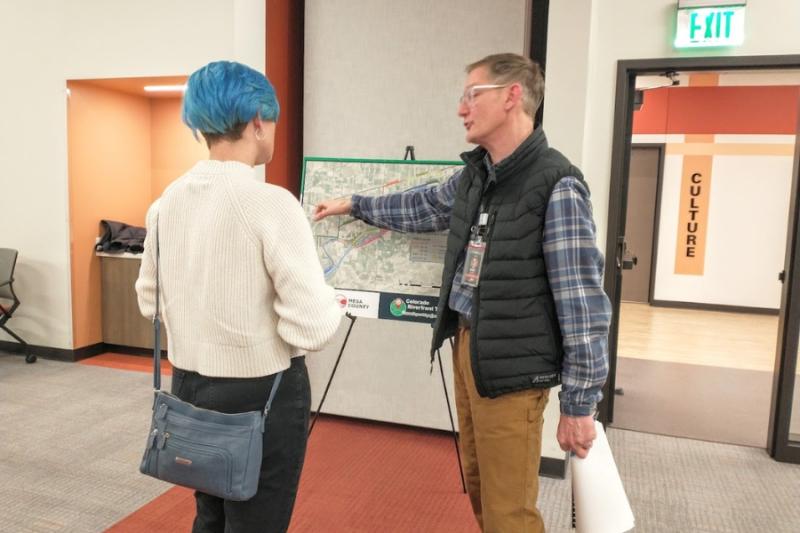 Three people facing a man pointing at a poster board with a map on it. 