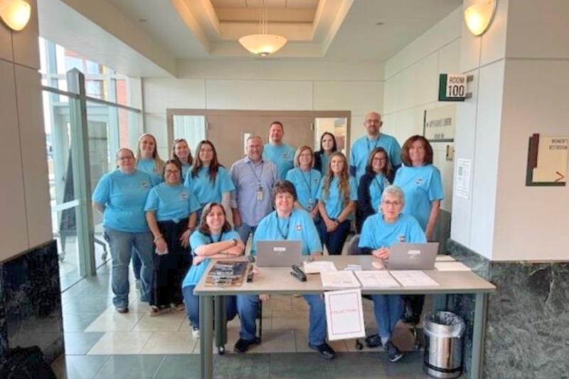 Large group photo. All individuals are wearing matching blue shirts and smiling.