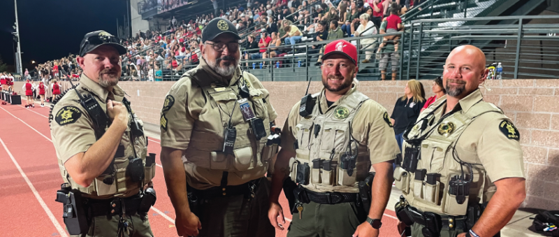 From left to right, MCSO School Resource Officers Deputy Garner, Sergeant Montez, Deputy T Rolbiecki, and Deputy Bunch stand on the track at Stocker Stadium during a high school football game.