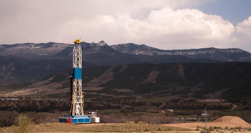 white and blue oil and gas rig on plateau with mountains in the background