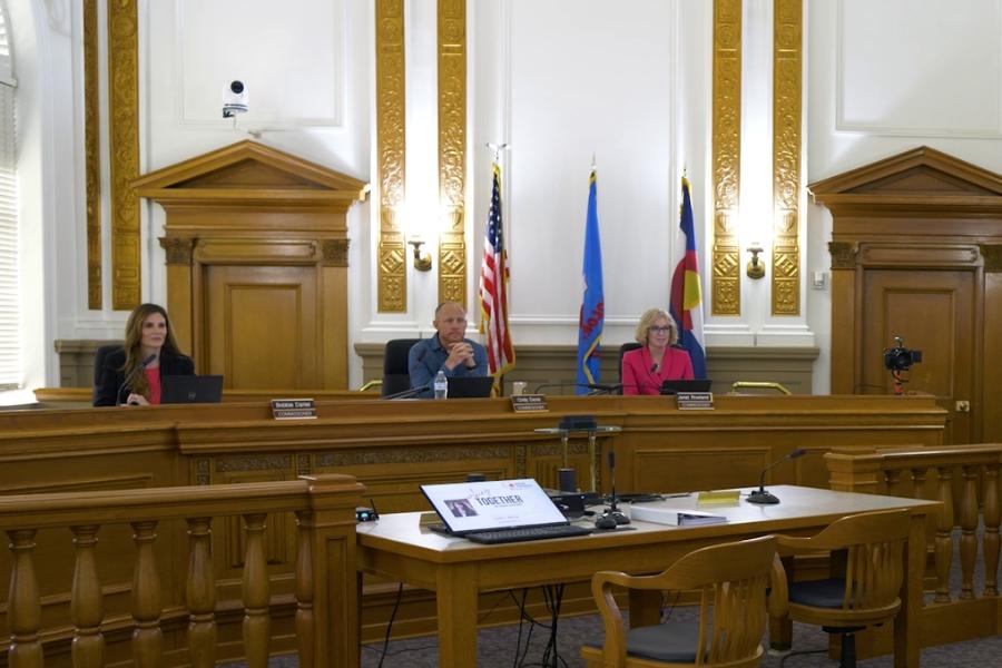 Three Mesa County Commissioners sitting in public hearing room. 