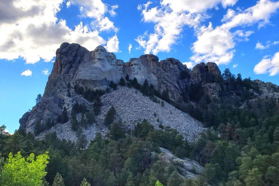 Mount Rushmore National Memorial in front of bright blue sky and white clouds. 