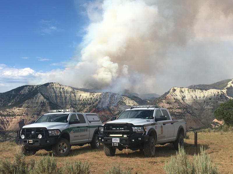 Photograph of Pine Gulch Fire area with Sheriff Vehicles and smoke clouds in the background.