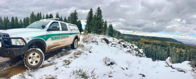 Photograph of Mesa County Sheriff Vehicle on Snow Covered mountain road with trees in the background