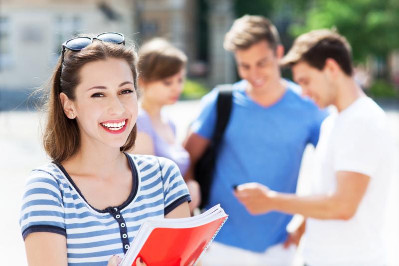 Photograph of a female College Student holding notebook with group of one female and two males in the background