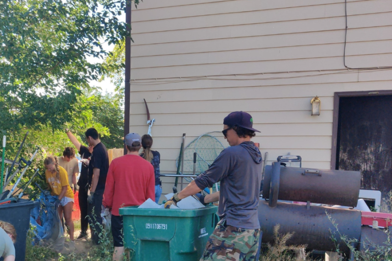 People cleaning up trash outside a home. 