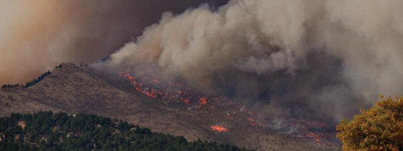 A mountain is on fire with grey brow smoke emanating from the flames.