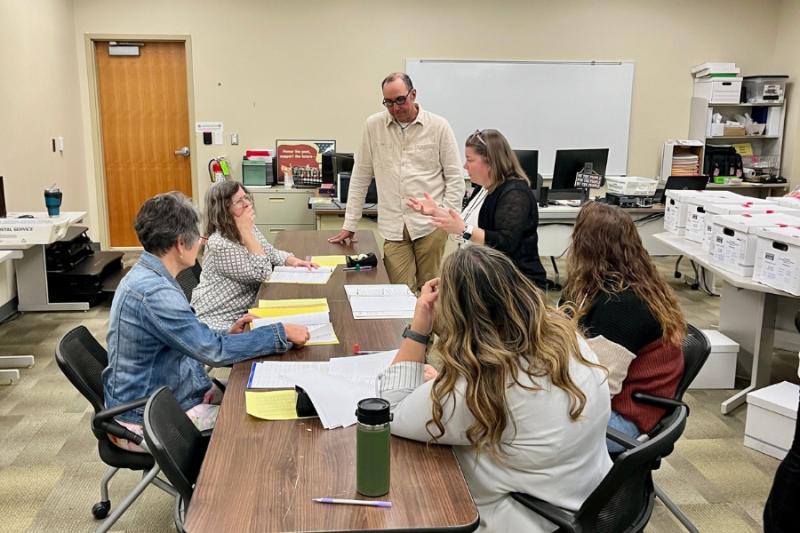 6 people sit around a table reviewing ballots. 