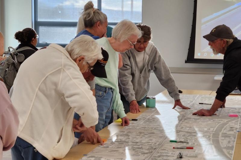 People stand around table with large map. 