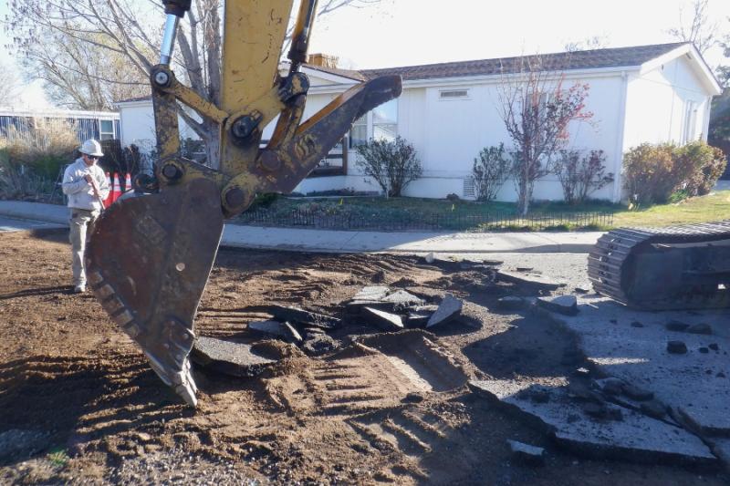 Heavy equipment digging into dirt on construction site with construction worker standing to the left. 