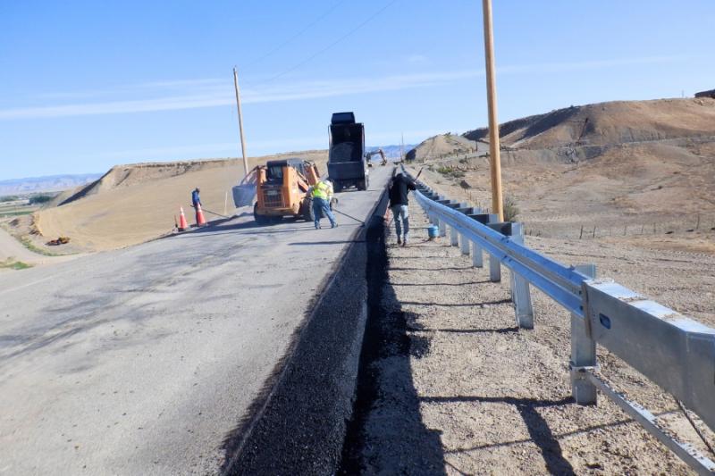 Construction workers adding new asphalt to side of road. 