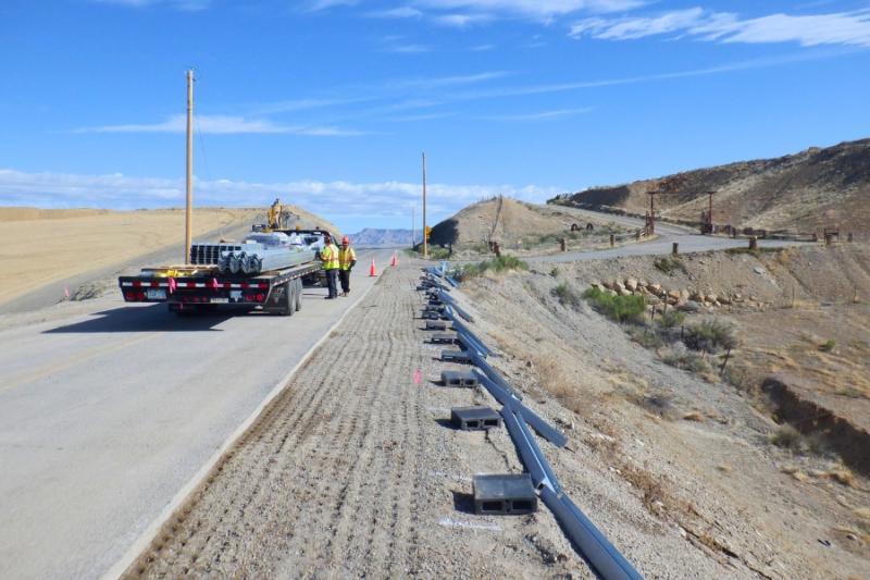 Guardrails broken down on side of road next to construction workers and truck with materials. 