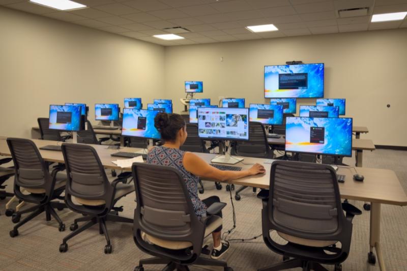 One woman sitting in a computer lab. 