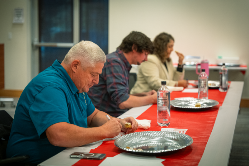 Three people sitting at a red table judging cookies.