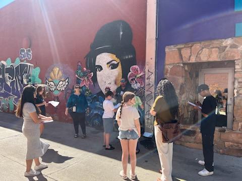 Seven people standing in a circle in front of a wall mural.
