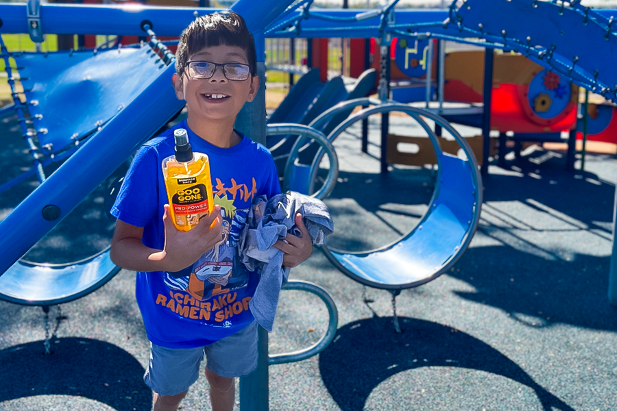 A third-grade boy stands with a bottle of cleaner and rags after removing graffiti