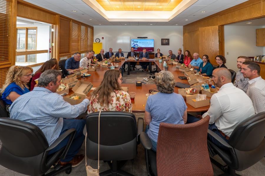 Large board room table with people sitting around it. 