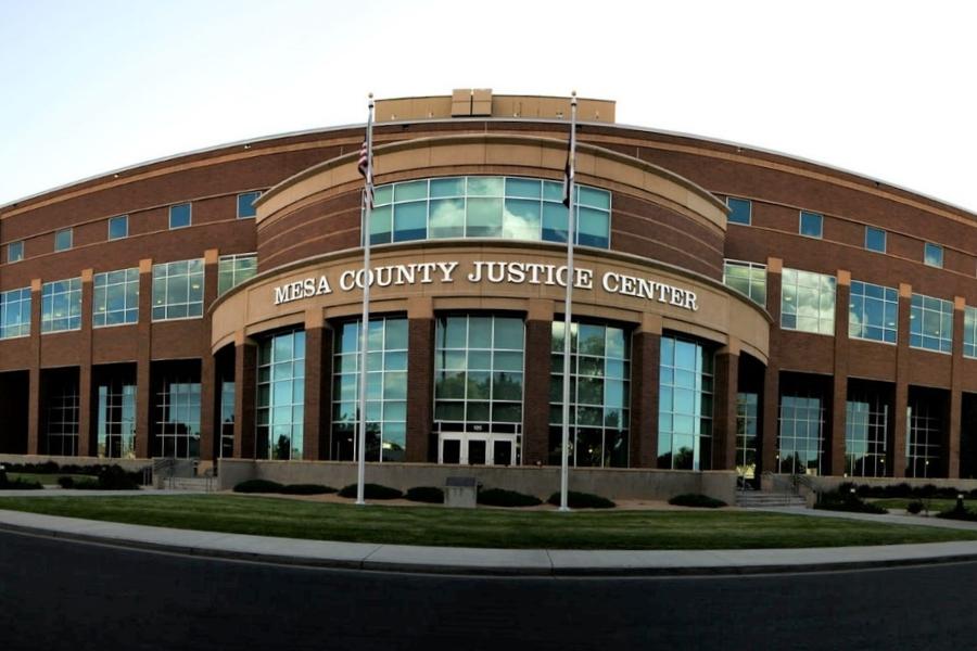 Front of Mesa County Justice Center. Brick building with white sign, windows, and two flags. 