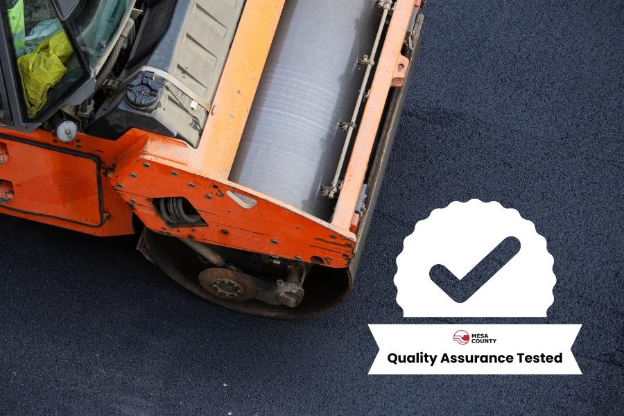 Orange heavy equipment rolling over fresh asphalt with white check mark element reading, Quality Assurance Tested. 