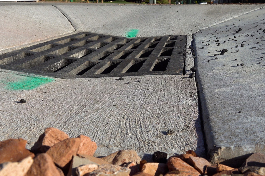 Close-up photo of a large drain grate surrounded by fresh concrete and red gravel.