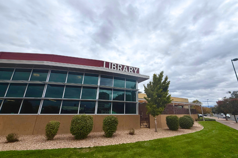 Photo of the outside of the Central Library in Grand Junction. The front of the building has tall glass windows and red siding with the word “library” in large letters above the windows.
